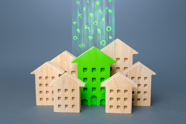 7 wooden houses of different sizes, the one centre in the image is green with small icons related to netzero flowing out of the top of it.